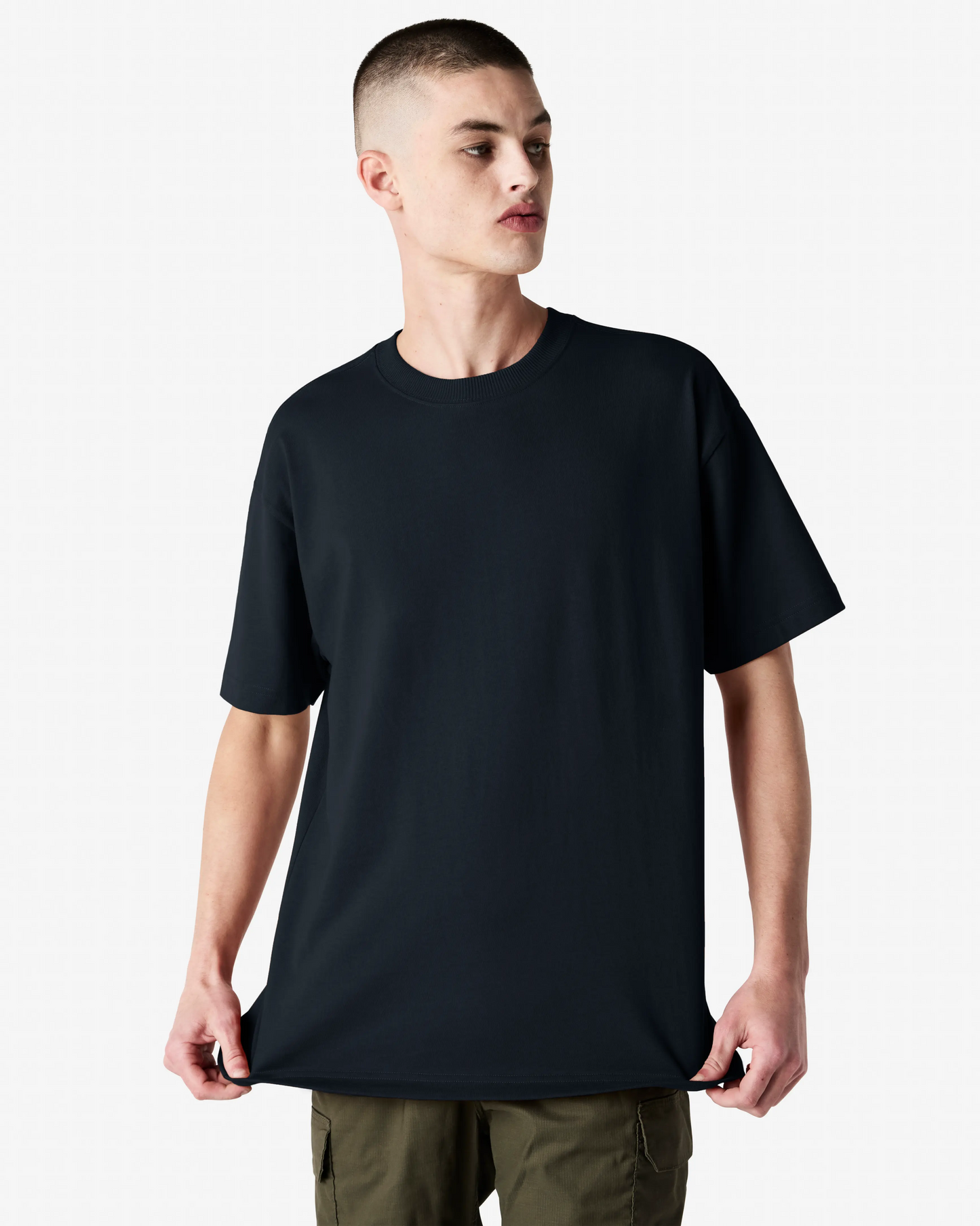 Male model wearing black American Apparel 9001 Super Heavyweight Tee, holding the hem to show relaxed oversized fit-black